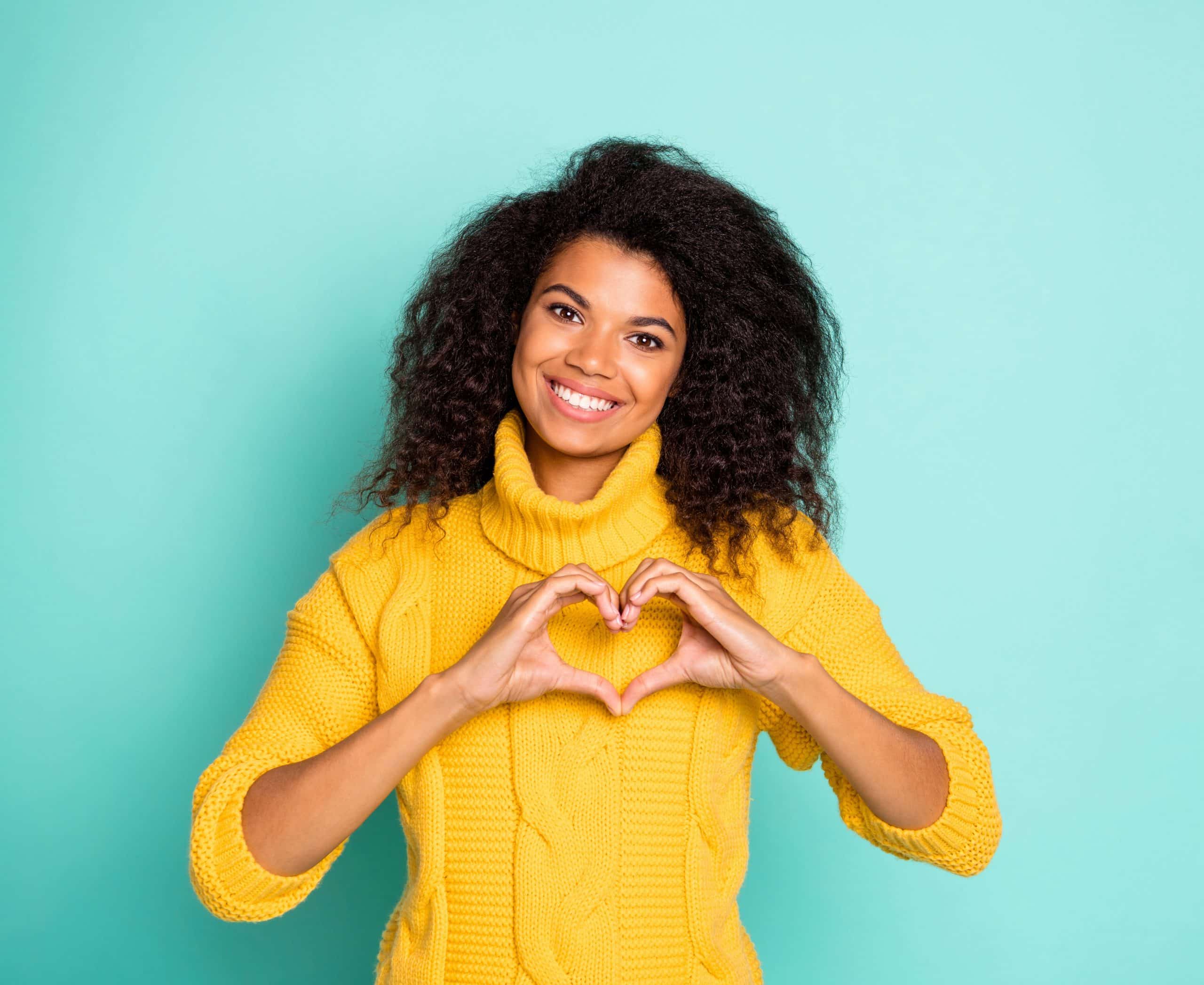 Photo of amazing dark skin lady holding hands in heart figure symbolizing, cardiac health care wear yellow knitted pullover isolated blue teal color background